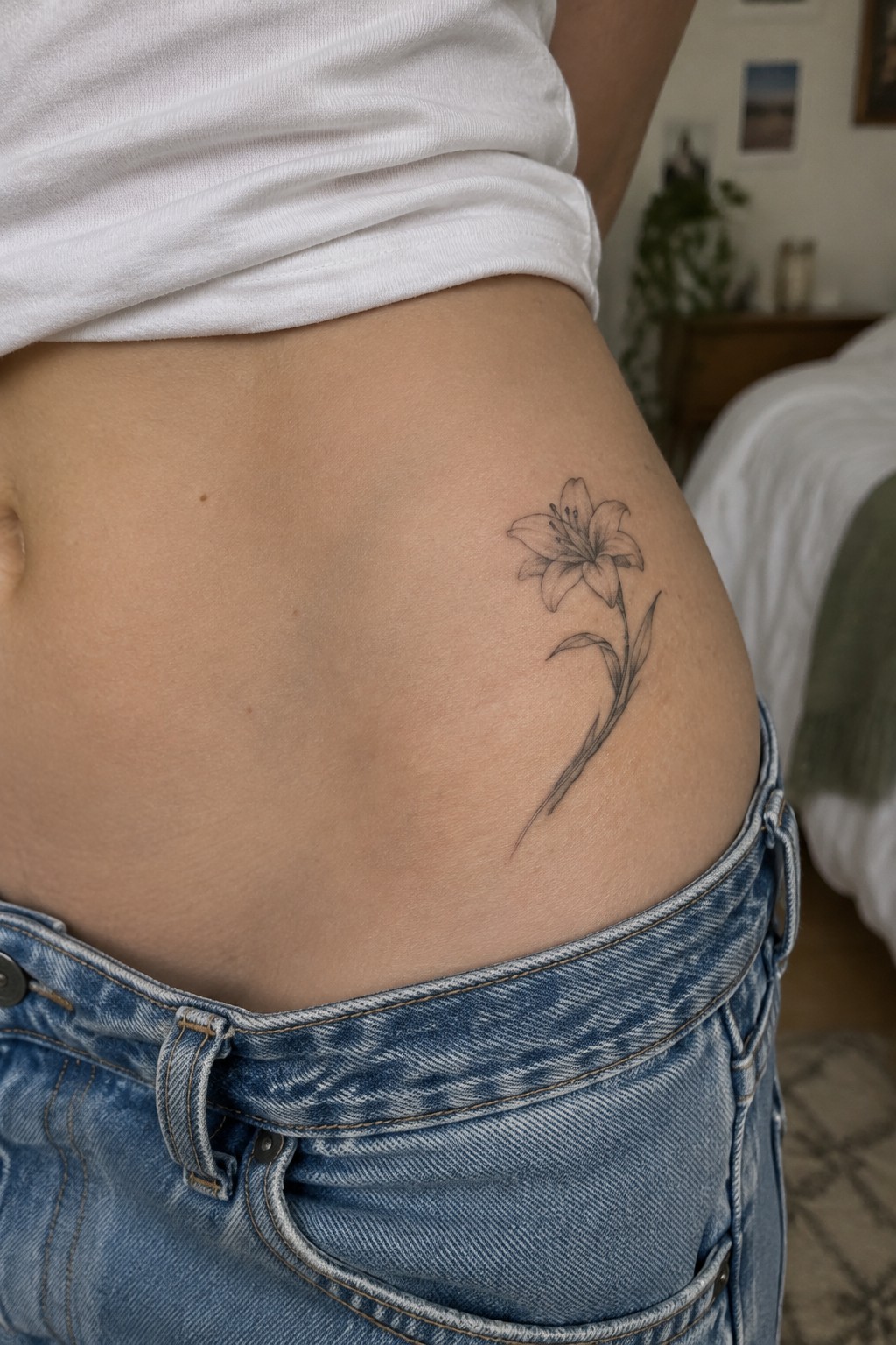 Lily tattoo on abdomen above blue jeans and white t-shirt in bedroom