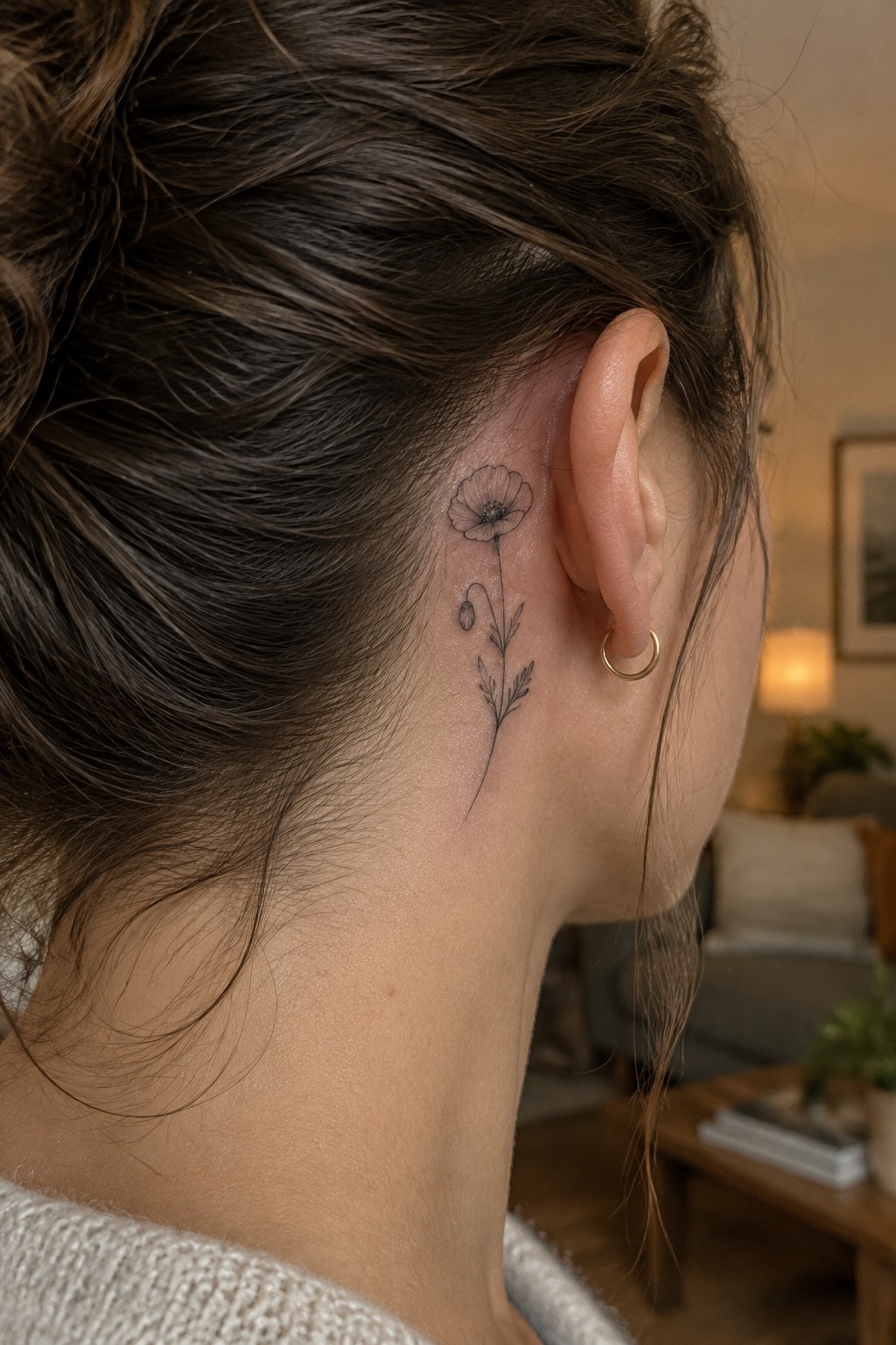 Brown hair in bun with delicate poppy tattoo behind ear and gold hoop earring