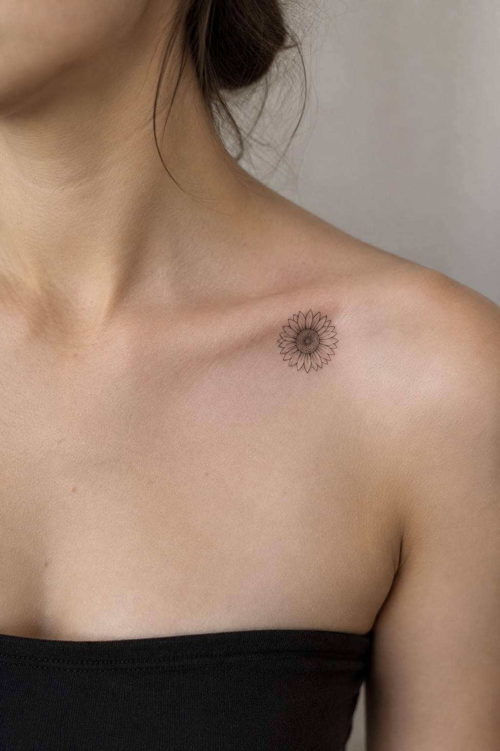 Minimalist fine line sunflower tattoo on a woman's upper chest near the shoulder