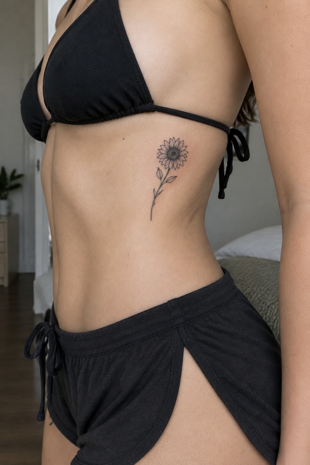 Woman's torso in black bikini with sunflower tattoo on ribs