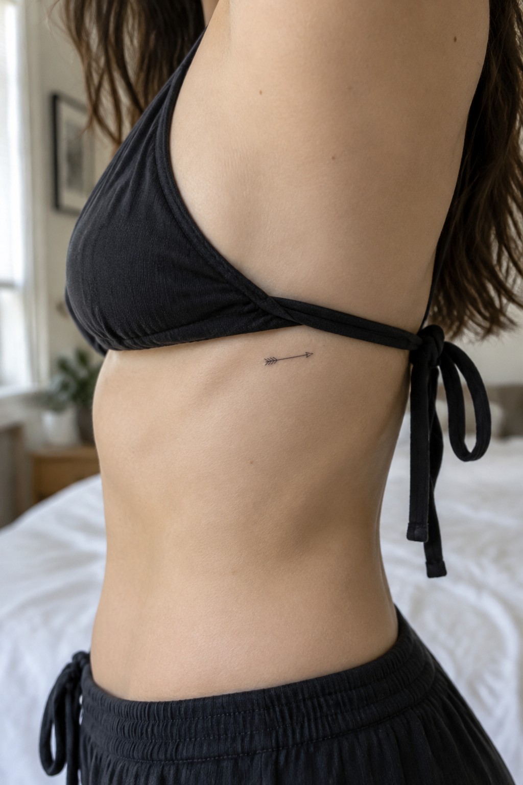 Small black arrow tattoo on the side of a woman's torso below the bikini top strap