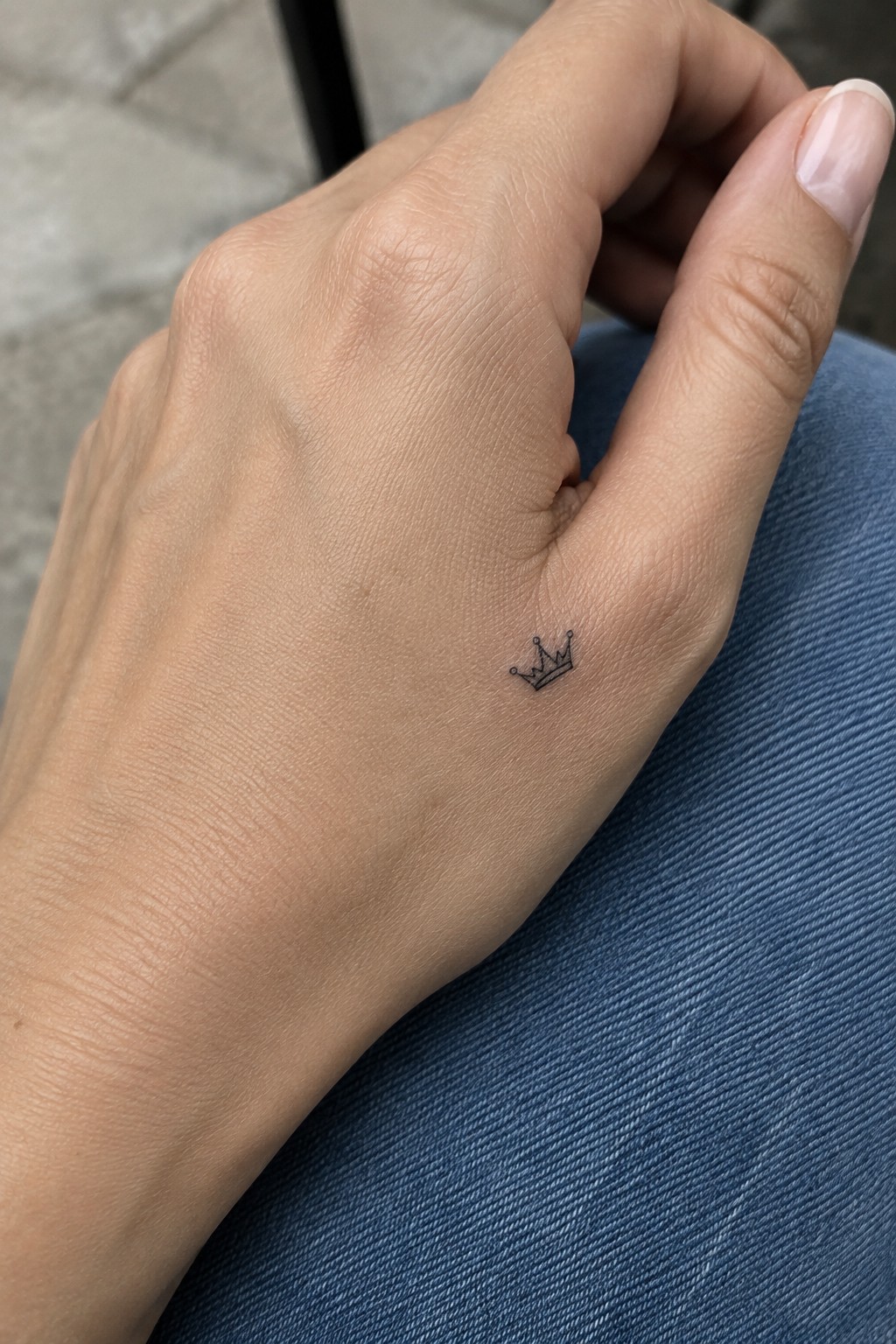 Hand with small crown tattoo resting on blue denim jeans fabric.