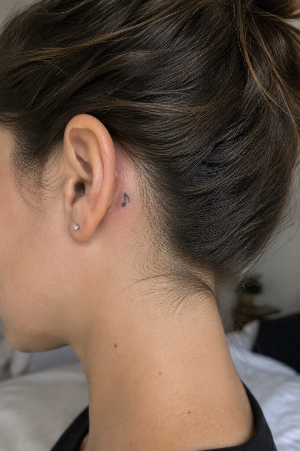 Woman with brown bun, musical note tattoo behind ear, and stud earring