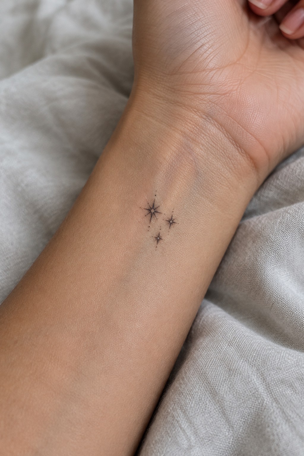 Fine line tattoo of three small star designs clustered on the inner wrist