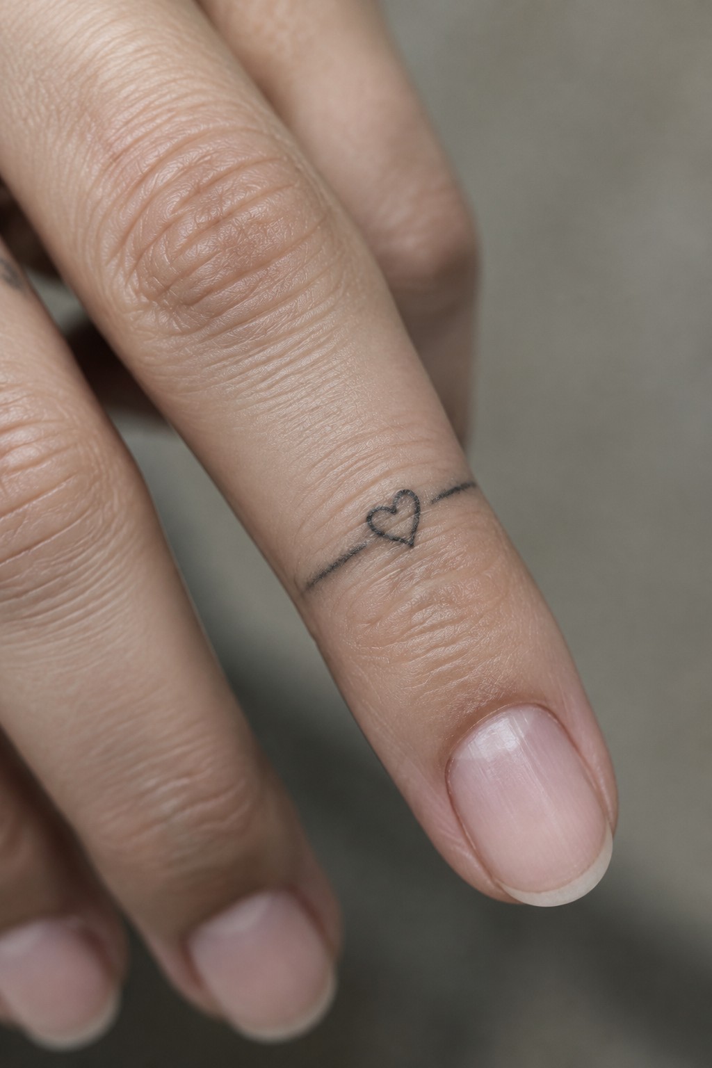 Close-up of light-skinned fingers with a small black heart-and-line tattoo.