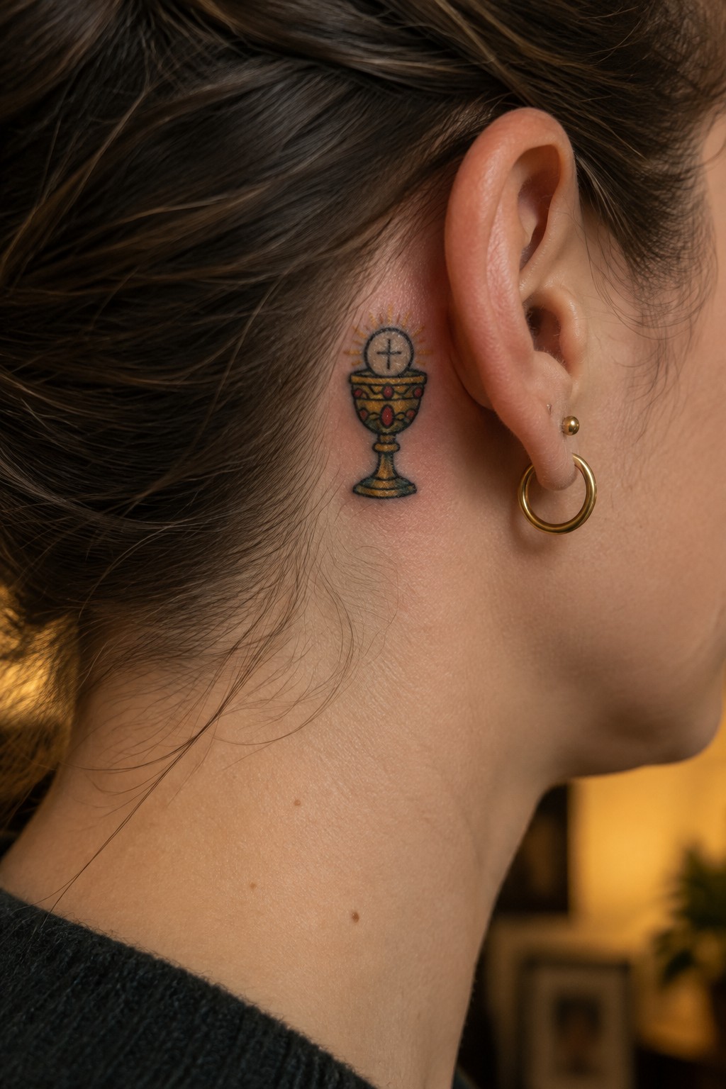 Ornate golden chalice tattoo with rays behind a woman's ear and gold earring