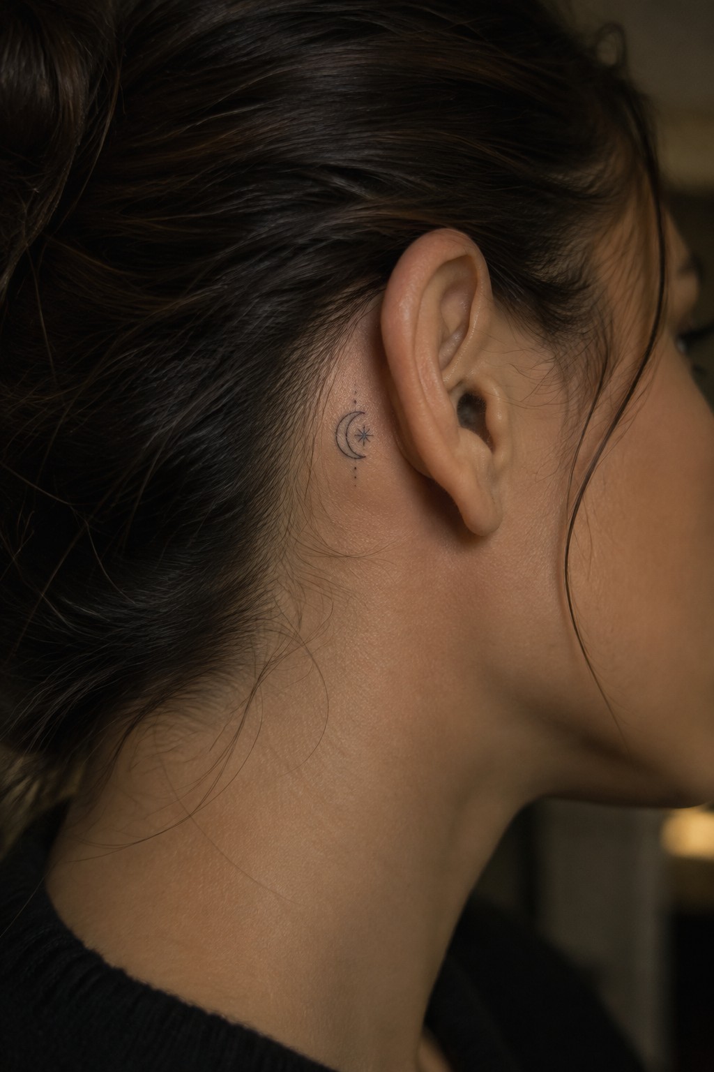 Woman with dark bun and crescent moon-star tattoo behind ear