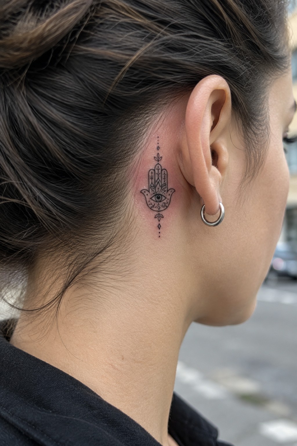 Small fine line hamsa tattoo with an eye placed behind a woman's ear