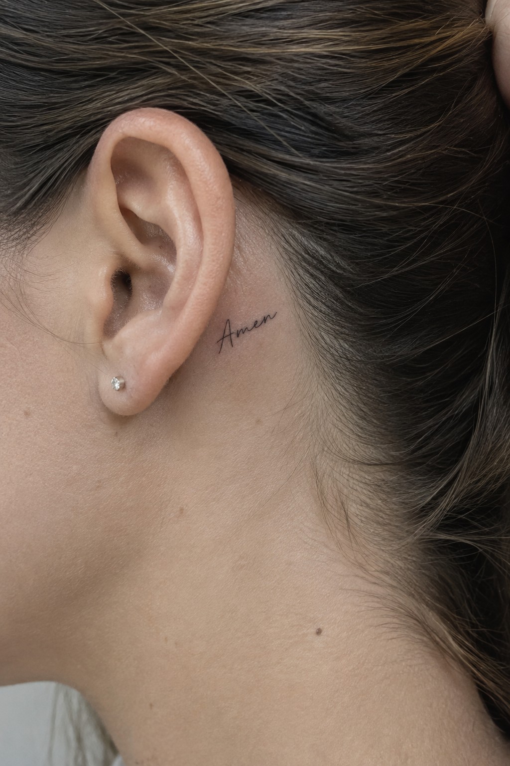 Close-up of ear with diamond stud earring and black cursive