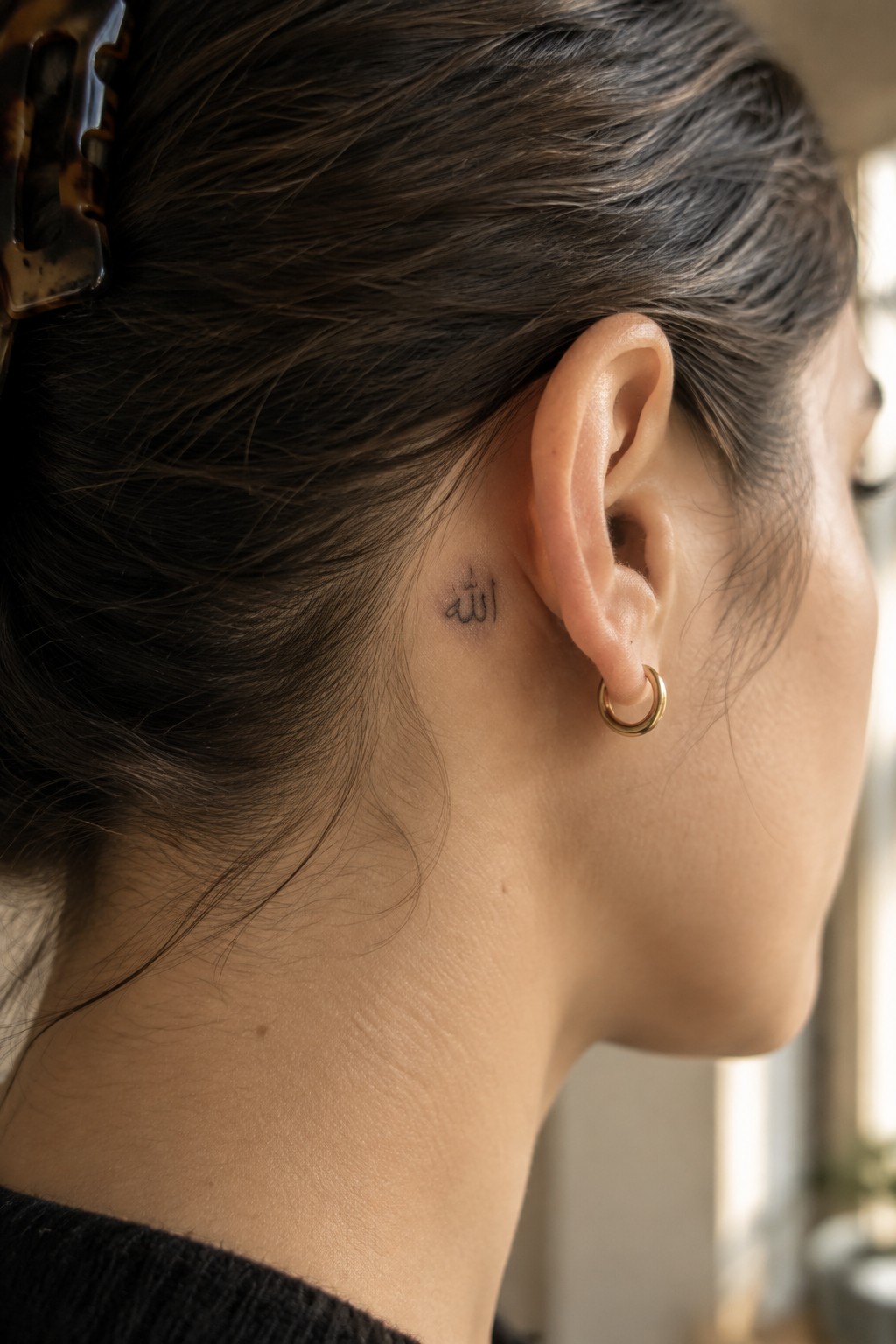 Dark-haired woman with Arabic tattoo behind ear and gold hoop earring