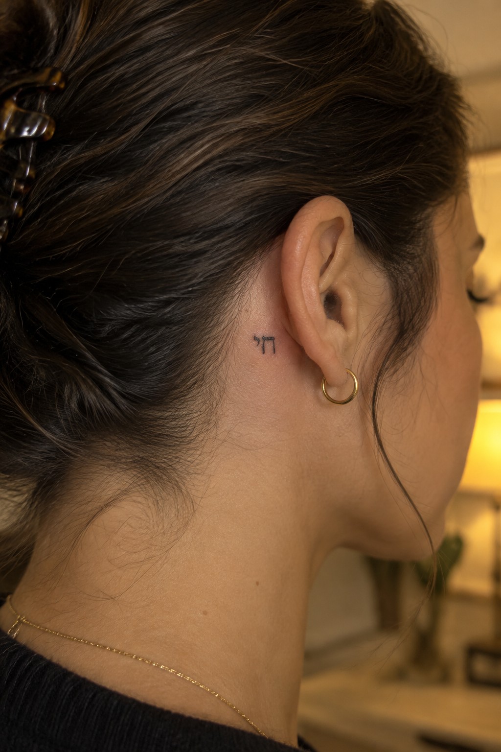 Woman's neck with small Hebrew tattoo behind ear, gold hoop earring and necklace