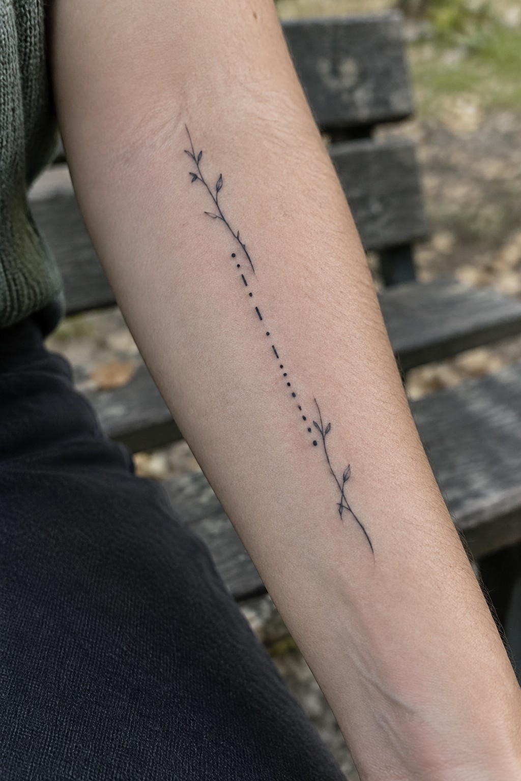 Delicate black plant stem tattoo with leaves and dots on forearm
