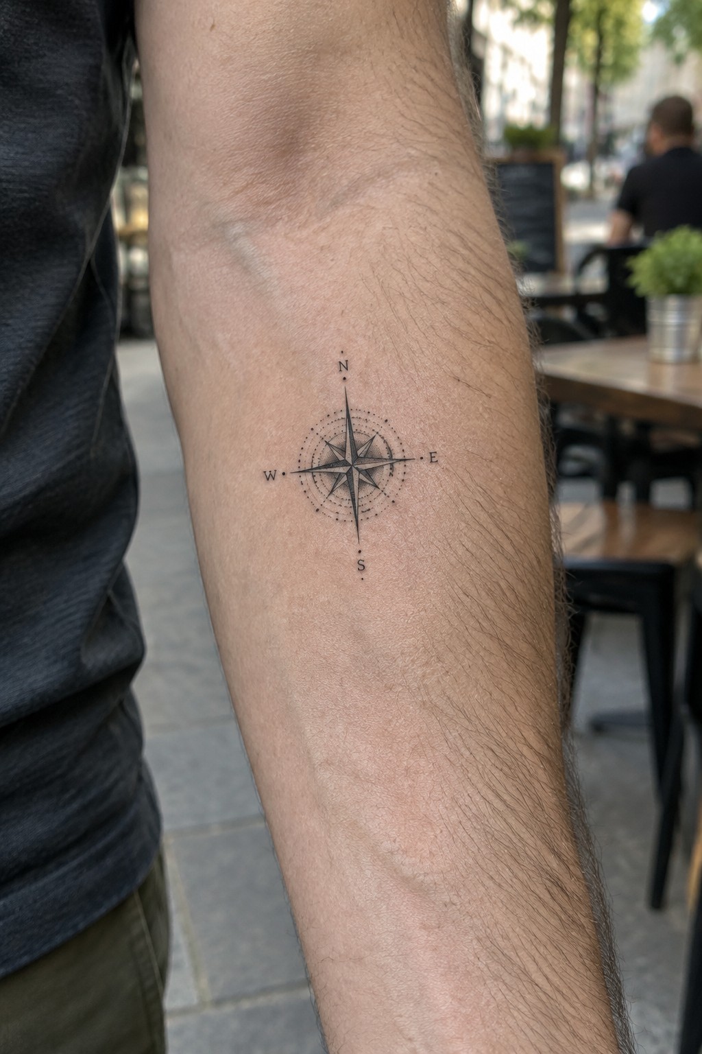 Small compass rose tattoo with N S E W labels in fine line style on the inner forearm.