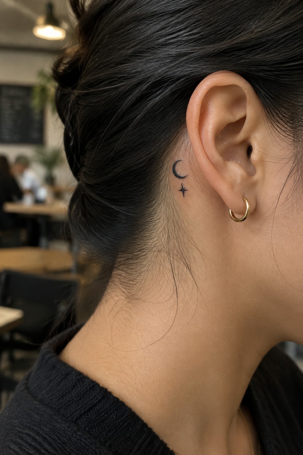 Dark hair in bun with moon-star tattoo behind ear and gold hoop earring