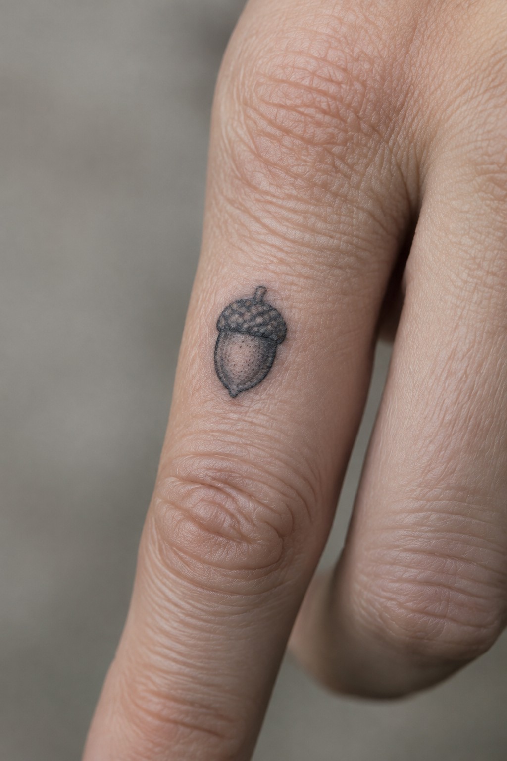 Small black-and-gray acorn tattoo on a wrinkled finger pad