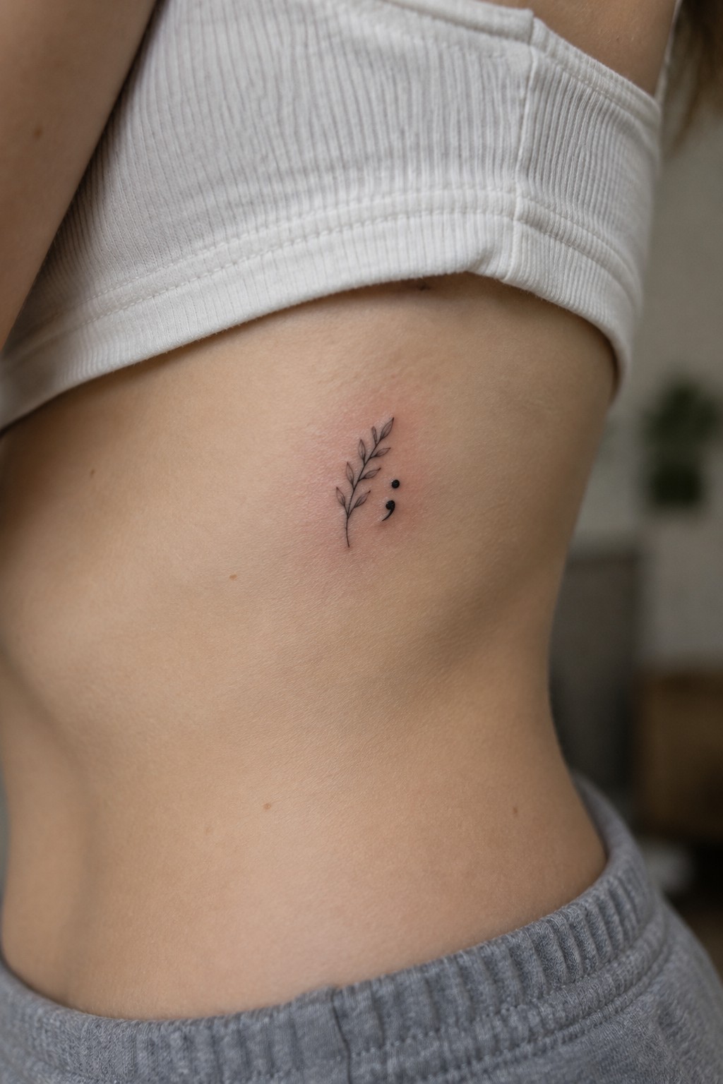 Semicolon and leafy branch tattoo on ribcage under white crop top
