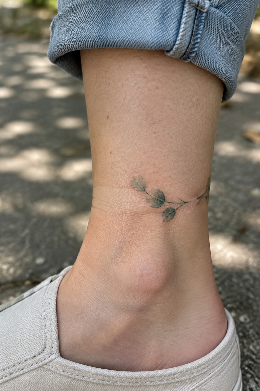 Small leafy branch tattoo on ankle with cuffed blue jeans and white shoe