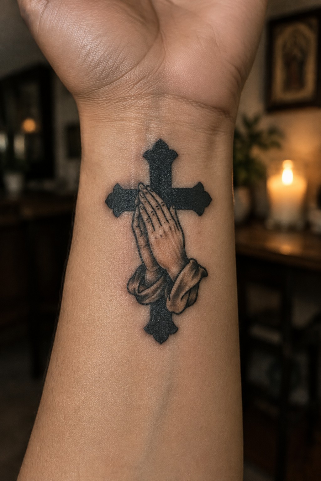 Black cross tattoo with realistic praying hands and draped cloth on wrist.