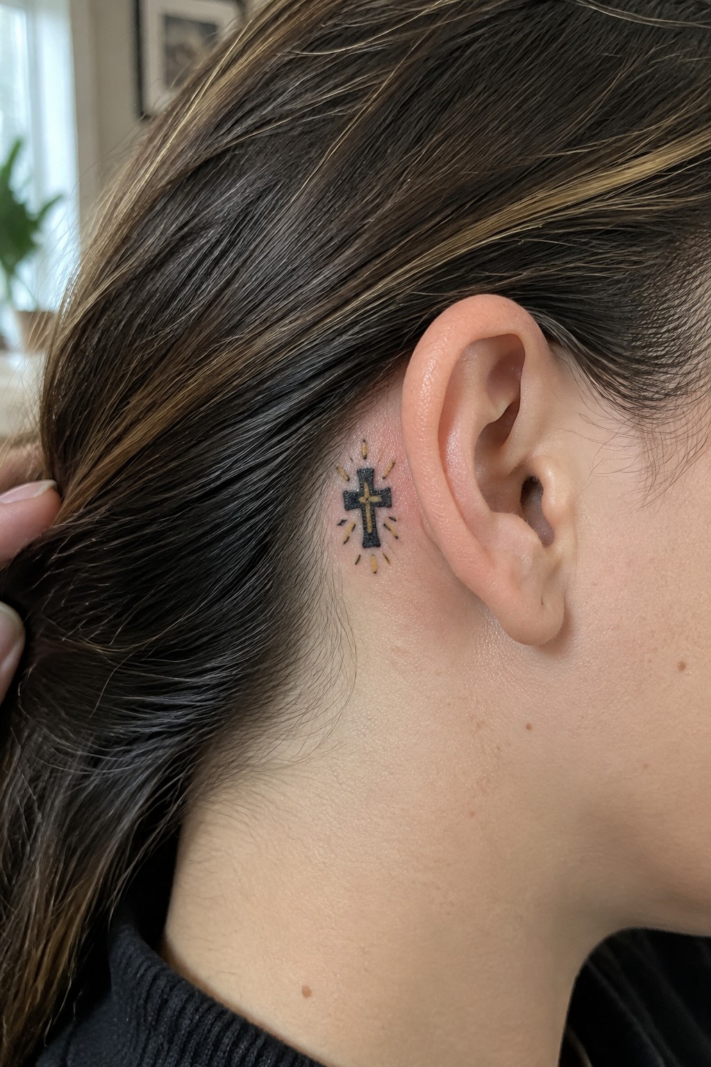 Black cross tattoo with yellow rays behind ear, brown hair pulled back