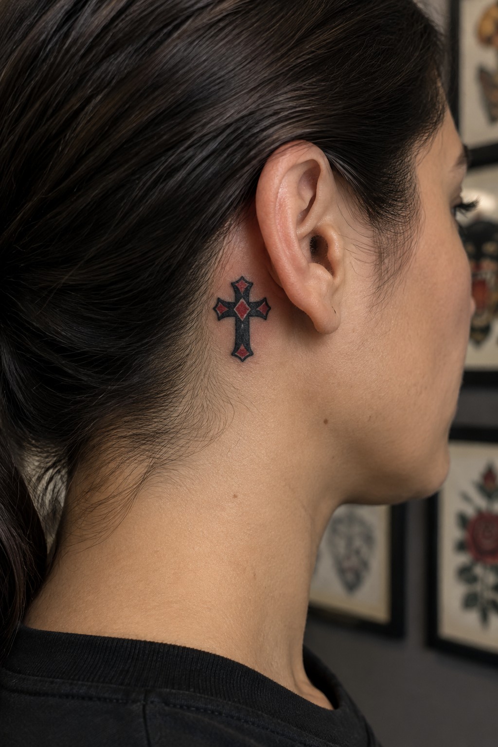 Small American traditional cross tattoo with red accents placed behind the ear on the side of the neck