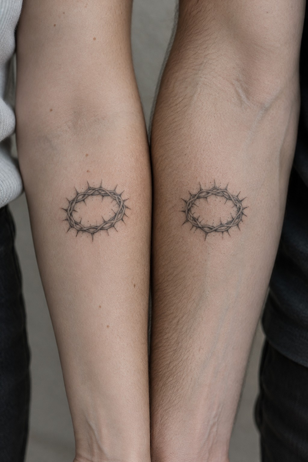 Two forearms with matching crown of thorns tattoos, light and dark skin tones.