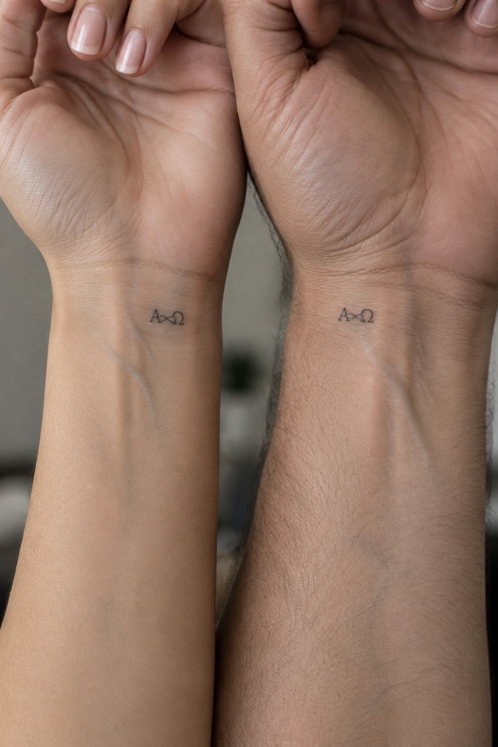Two palms-up hands showing matching black A∞2 wrist tattoos on light and dark skin.