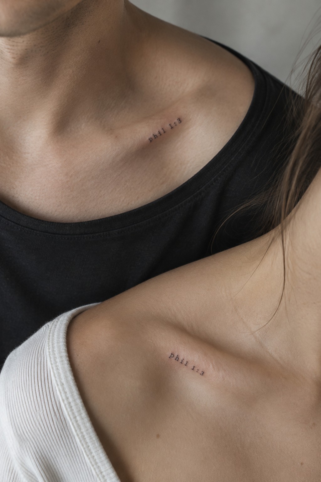 Couple displaying matching 'phil 1:3' tattoos on collarbones, black tank and white top