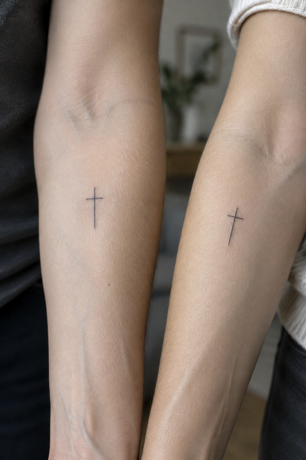 Two forearms with matching small black cross tattoos, dark and light sleeves visible.
