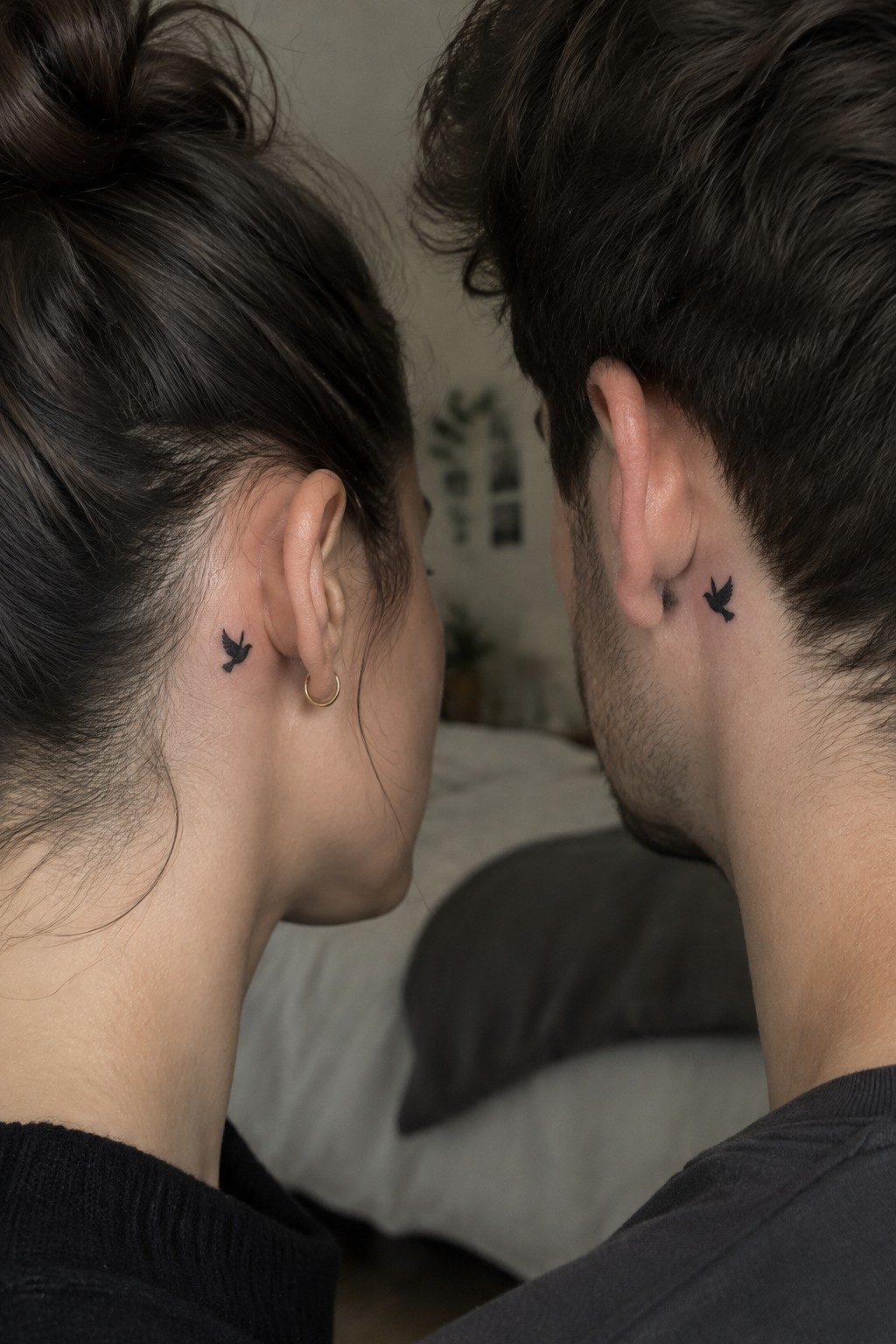 Couple with matching small black bird tattoos behind their ears in bedroom