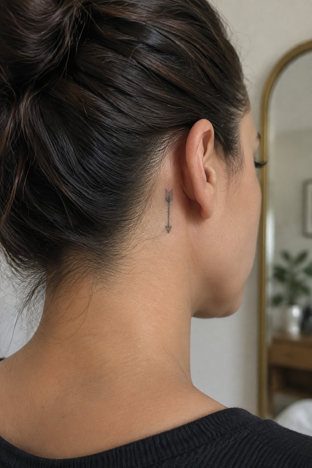 Small fine-line arrow tattoo behind a woman’s ear, pointing downward.