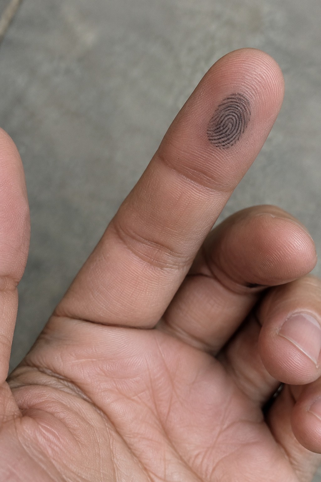 Small black fingerprint tattoo on the pad of a finger.