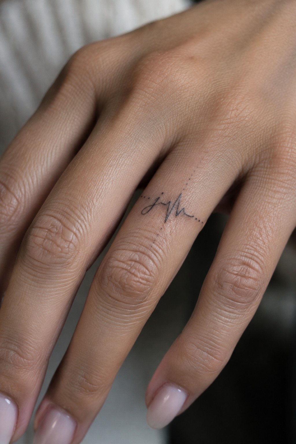Fine-line heartbeat tattoo with a small handwritten detail on the back of a finger.