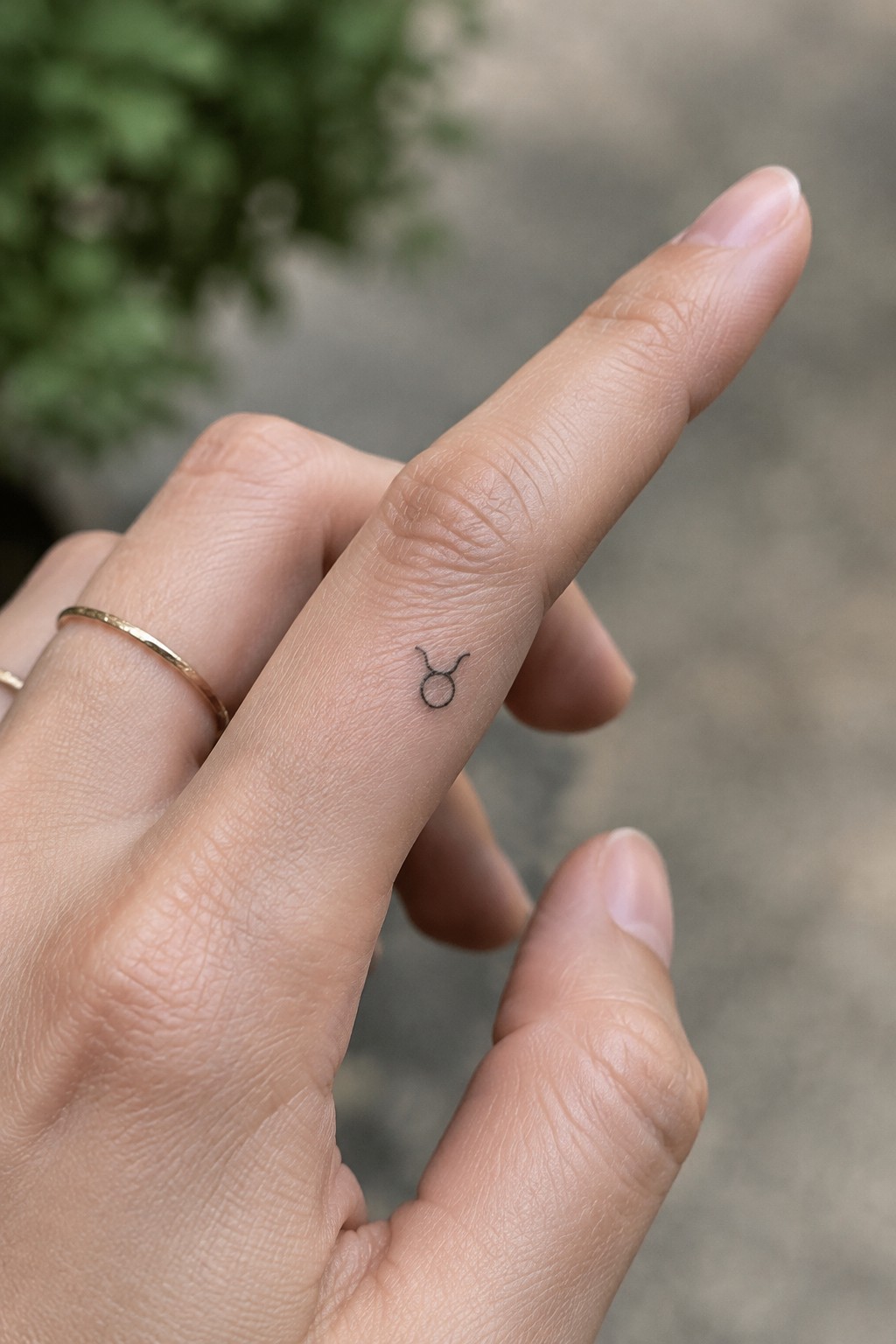 Small black Taurus symbol tattoo on the side of a finger.