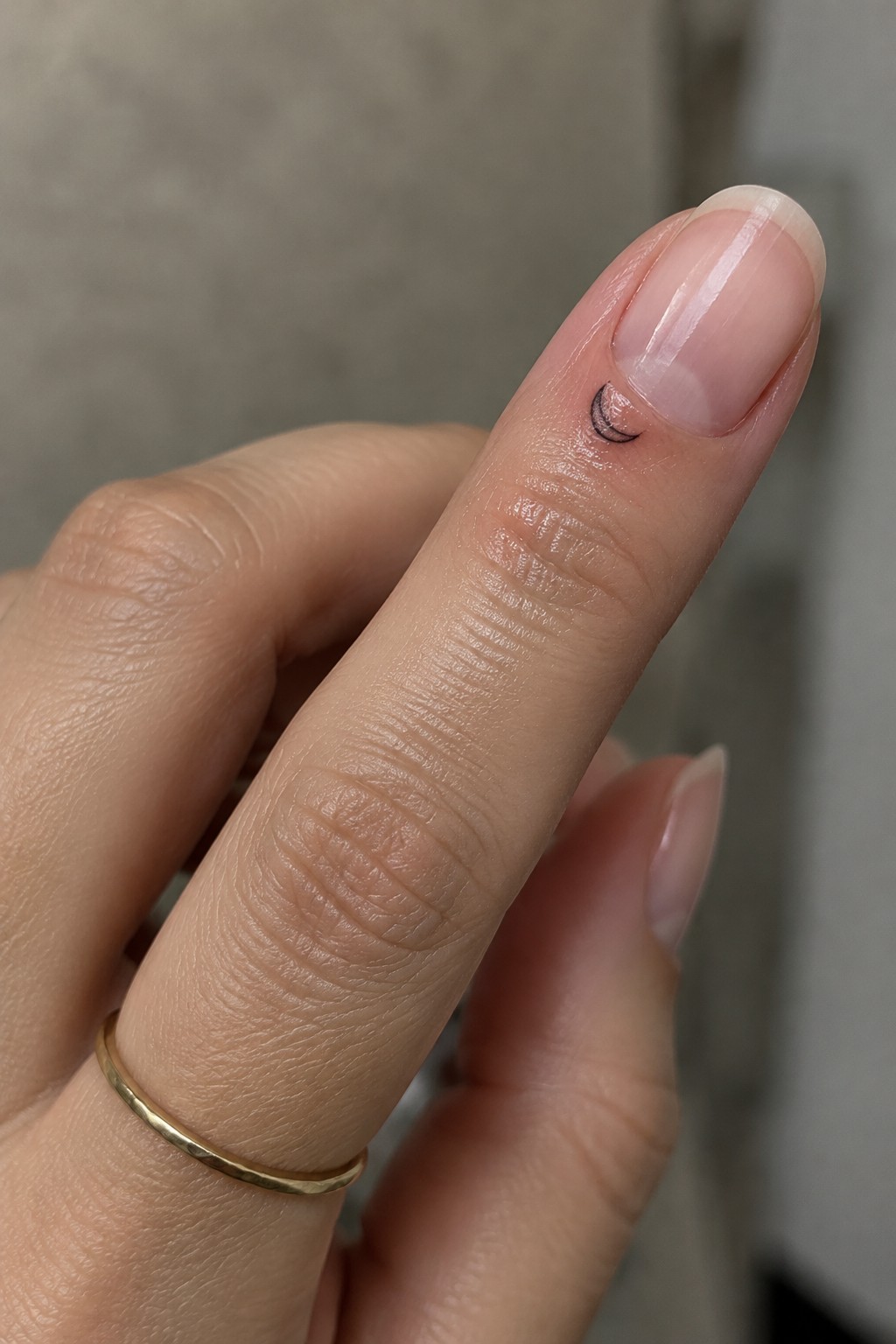 Small black crescent moon tattoo near the nail on a finger.