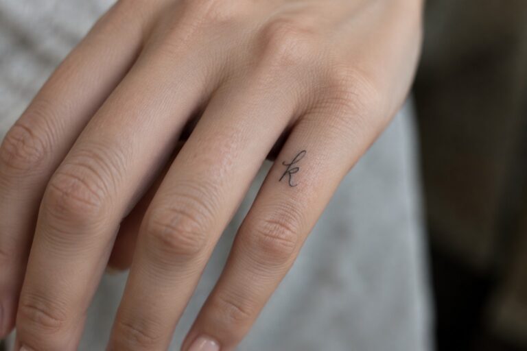23 Dainty Finger Tattoo Ideas for Women Centered Around Personal Symbols Small black cursive initial tattoo on the side of a finger.
