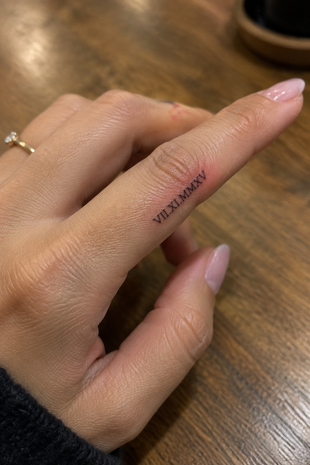 Fine black Roman numerals tattooed along the side of a finger.