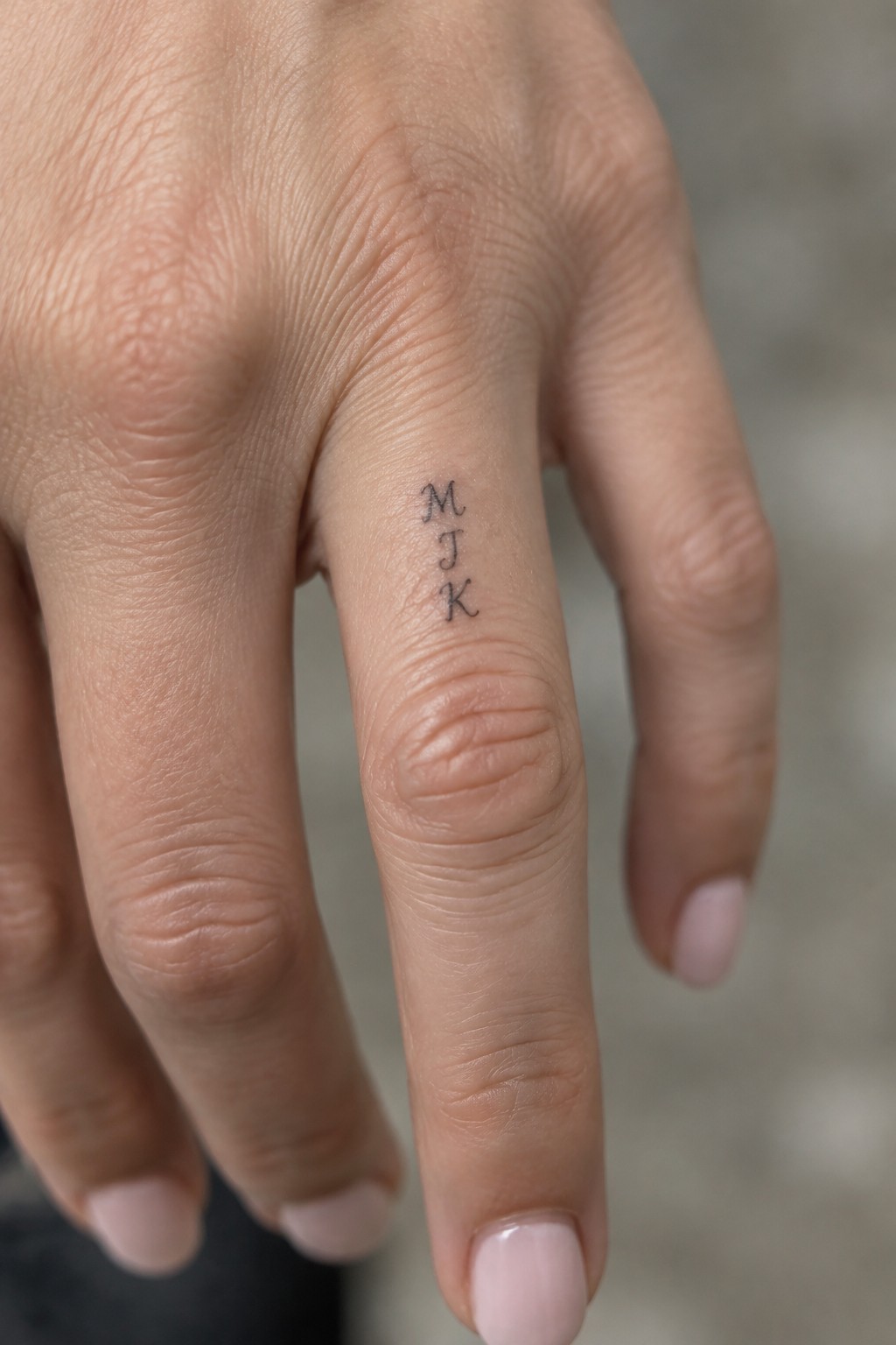 Three small black letters tattooed vertically on the upper section of a finger.