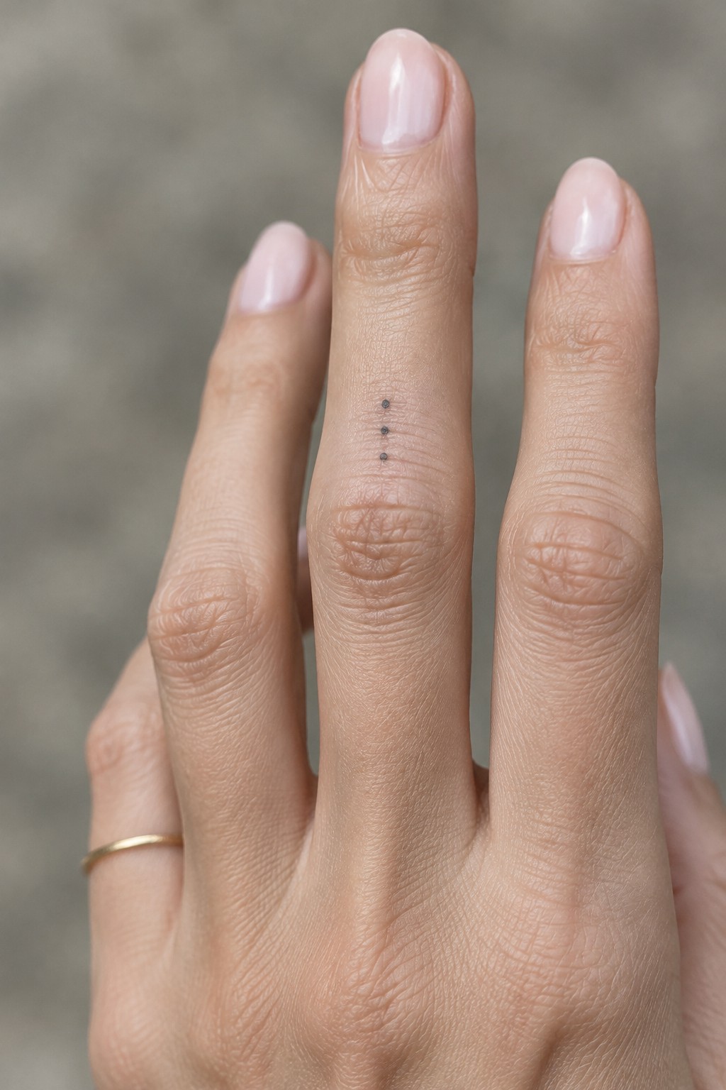 Three small black dots in a vertical line tattooed above the knuckle on a finger.