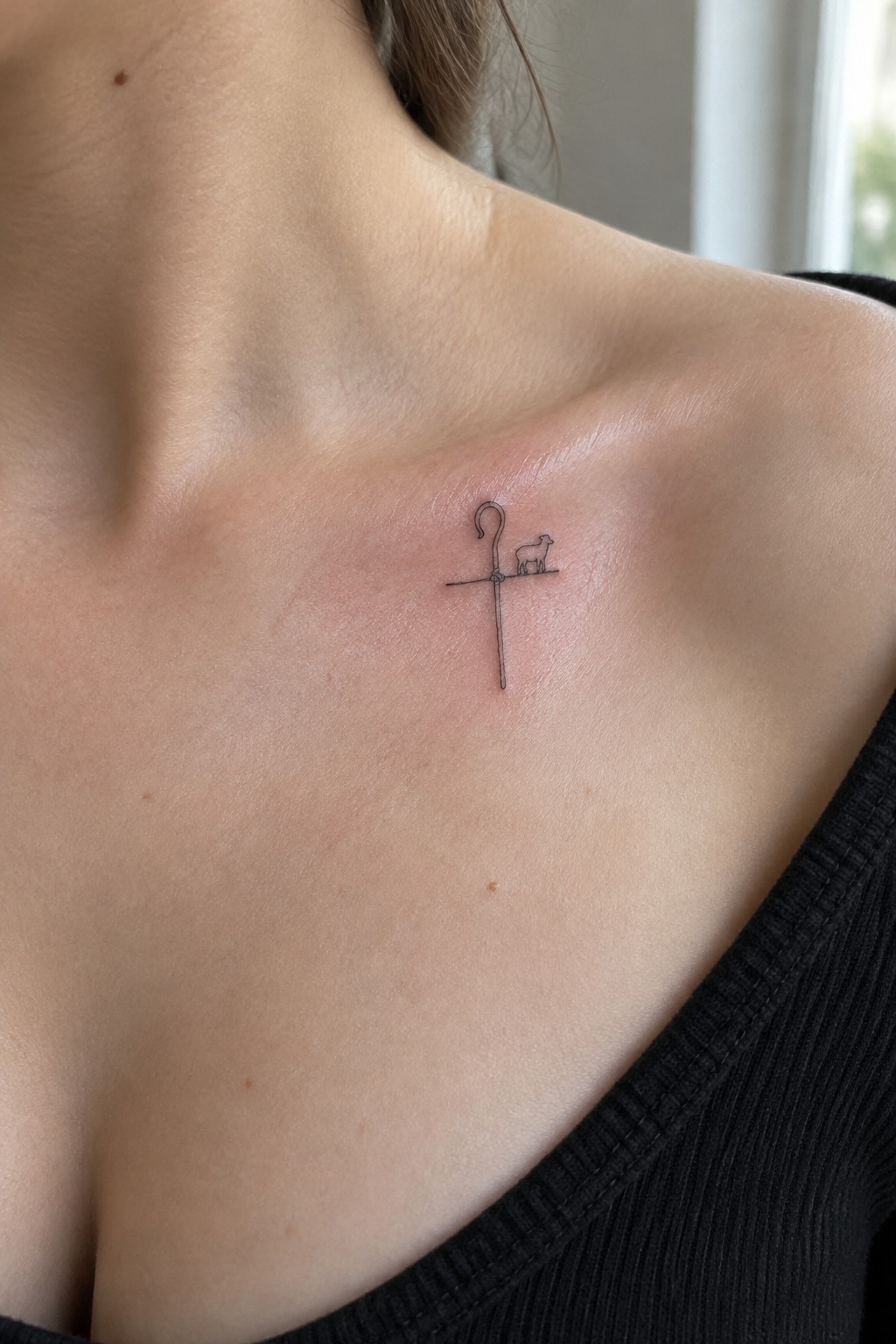 Minimalist black line tattoo of cross with shepherd's crook and lamb on chest