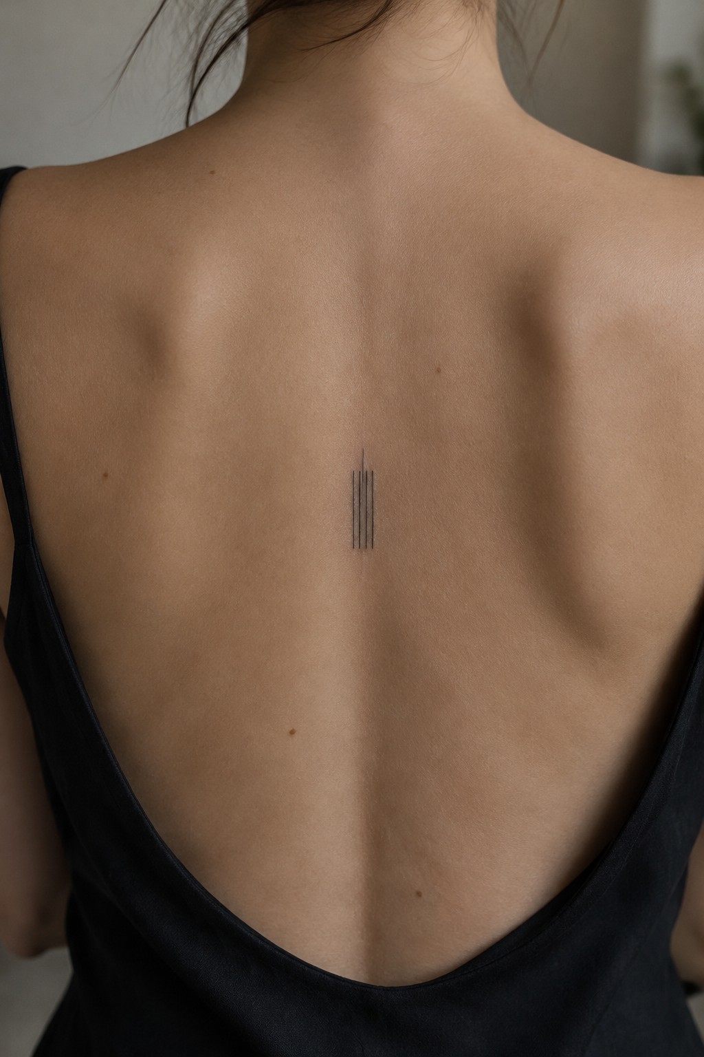 Woman's upper back with minimalist four-line tattoo above black low-back dress