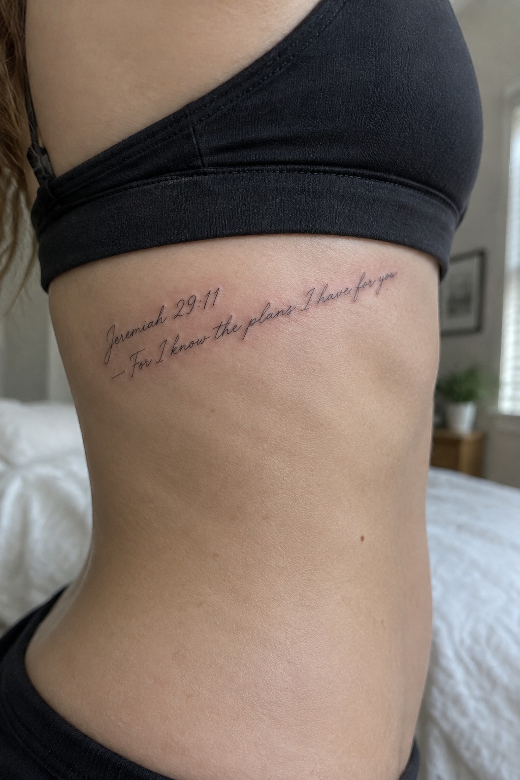 Woman's ribcage with Jeremiah 29:11 tattoo under black crop top in bedroom