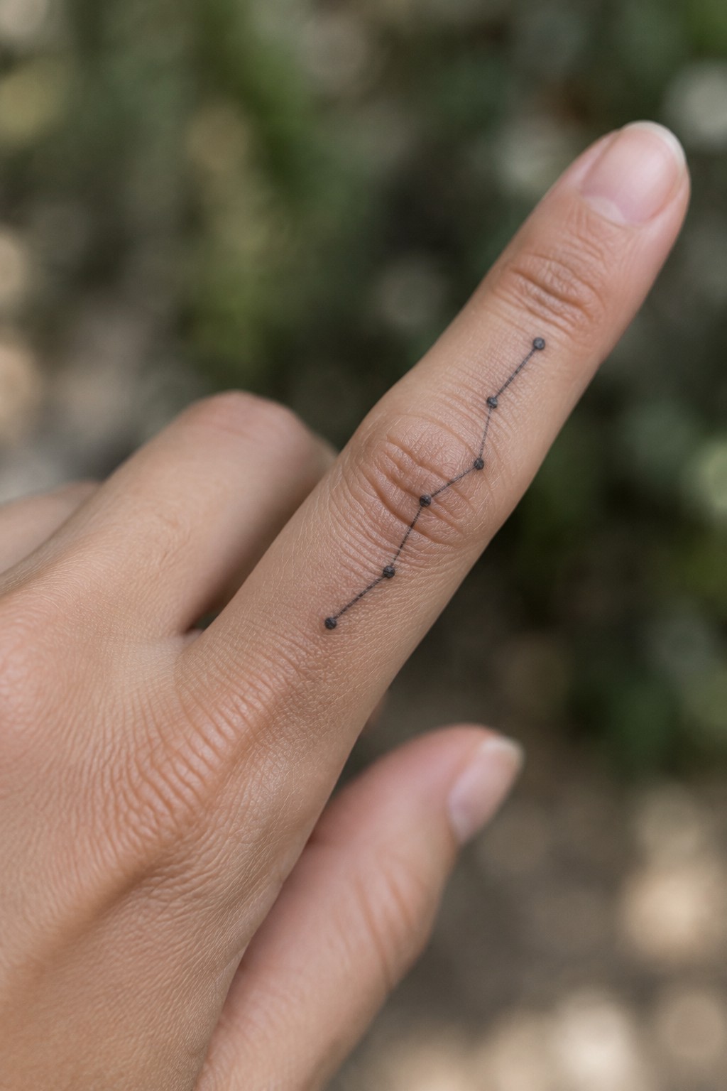 Fine-line constellation tattoo made of small dark dots connected by thin lines along a finger.