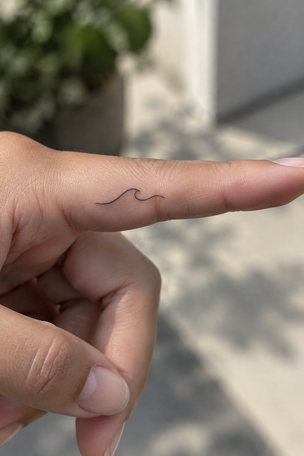 Small black fine-line wave tattoo on the side of an outstretched finger.