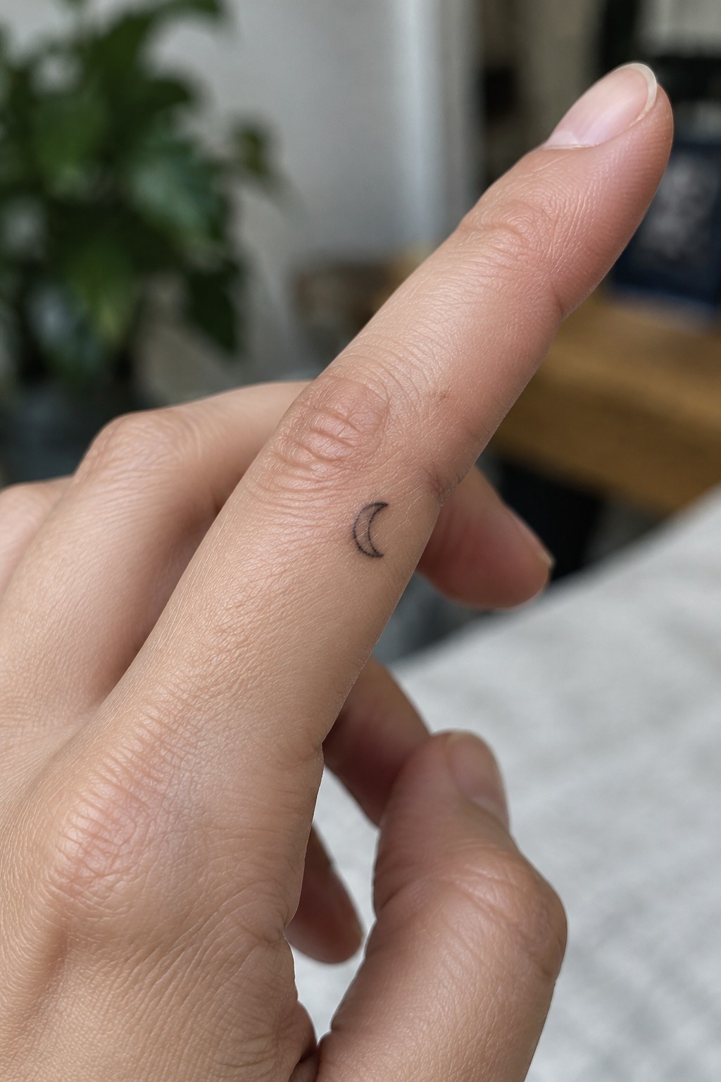 Small black crescent moon tattoo on the side of a finger.