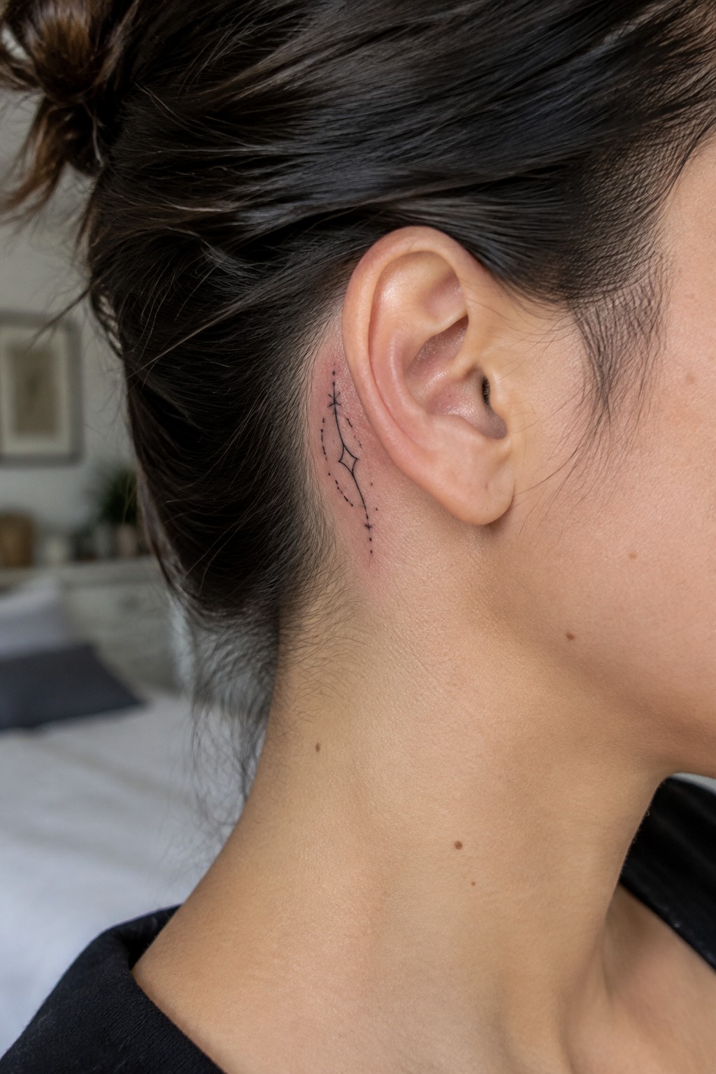 Fine-line tattoo of a star, diamond-shaped sparkle, and dotted trail behind a woman's ear.