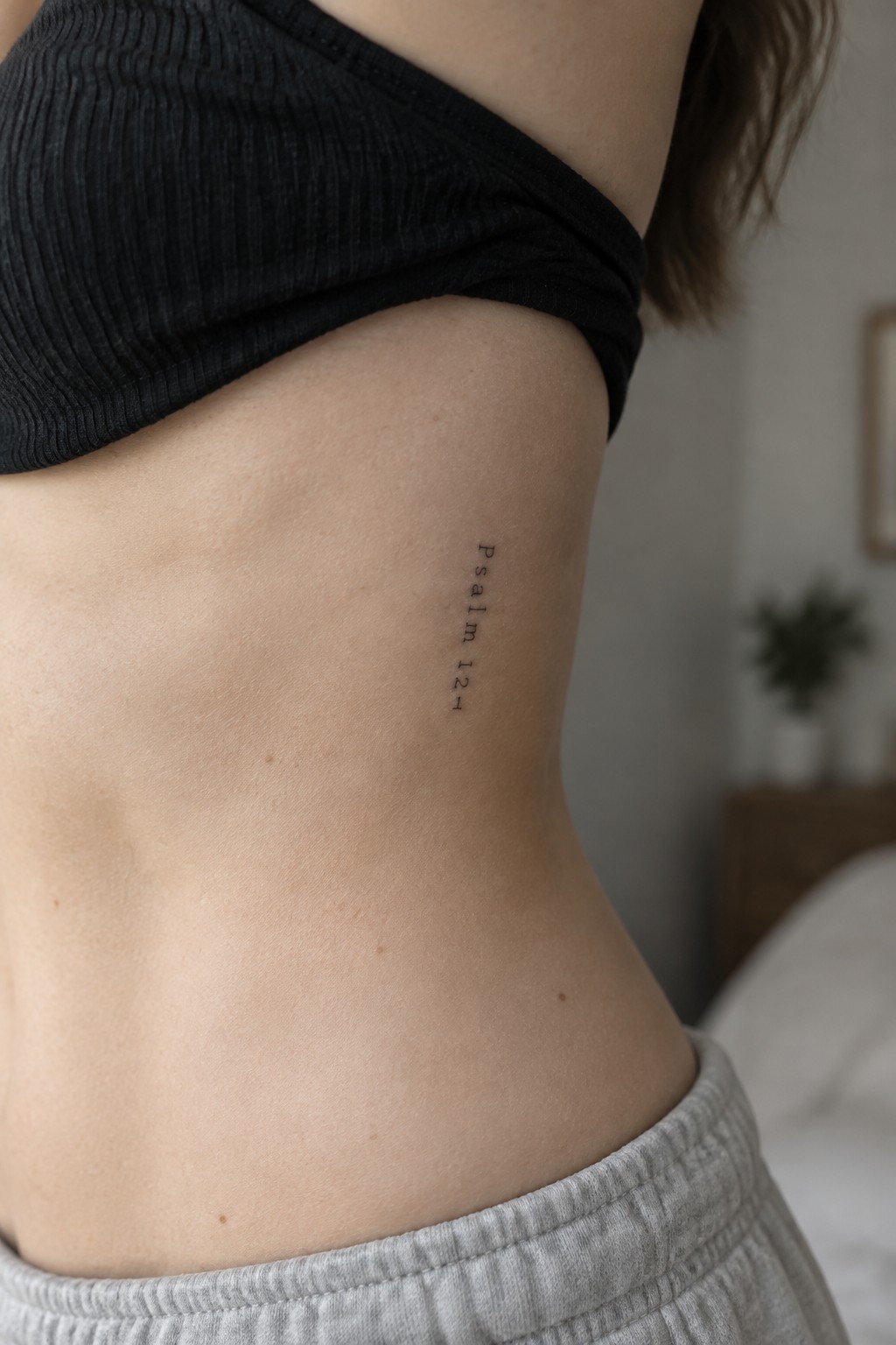 Fine line vertical tattoo of Psalm 121 on the side of a woman's torso under the ribcage