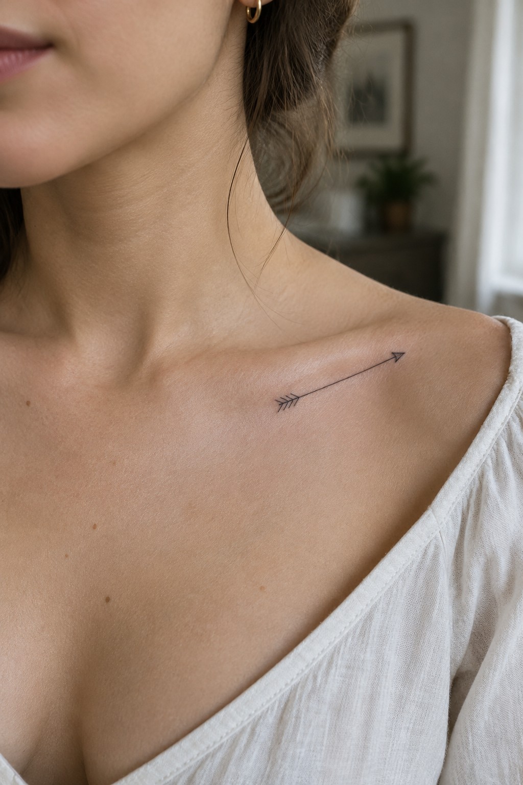 Small black fine-line arrow tattoo with feathered fletching on a woman’s collarbone.