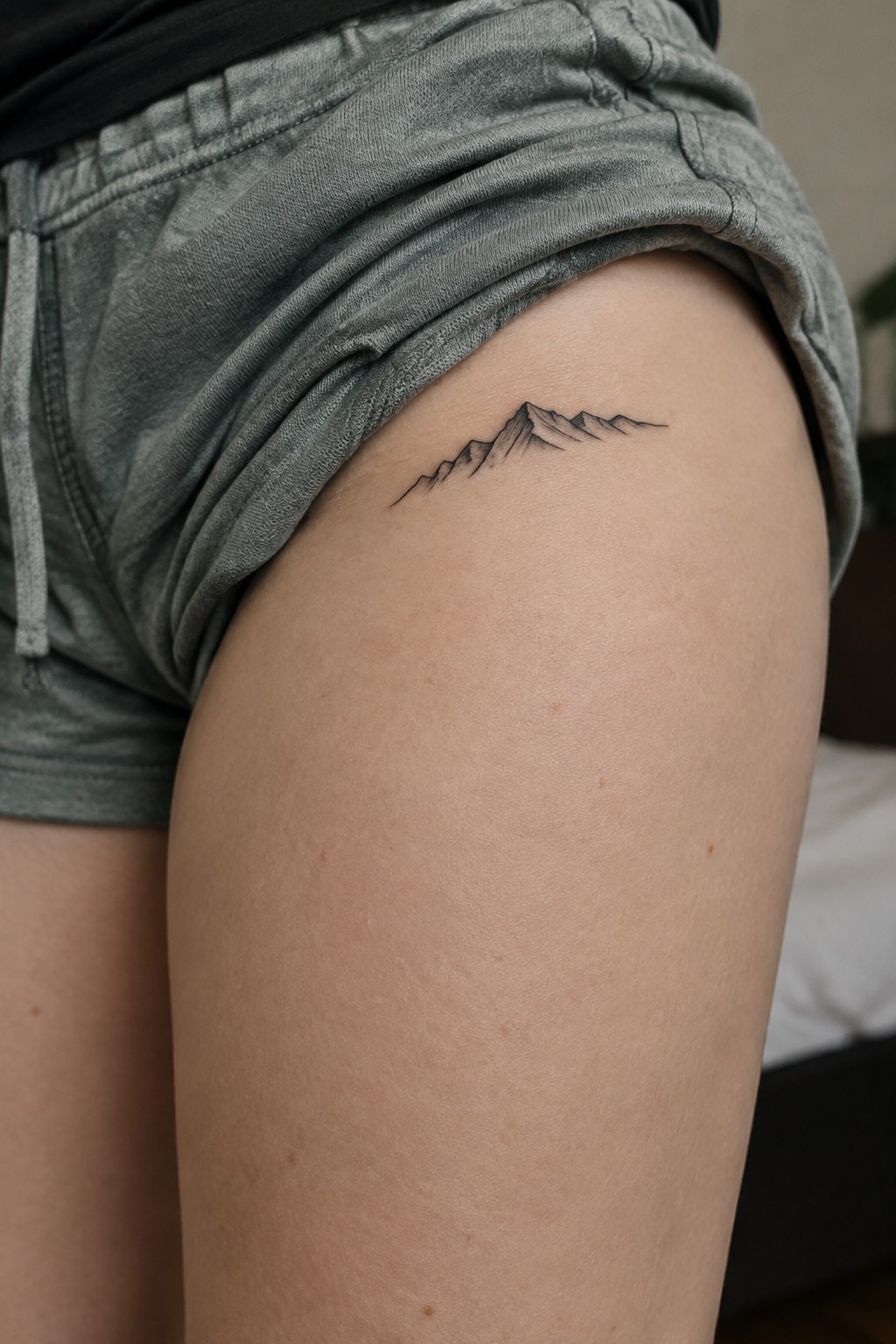Small fine-line mountain range tattoo on the upper thigh near the edge of rolled-up shorts.