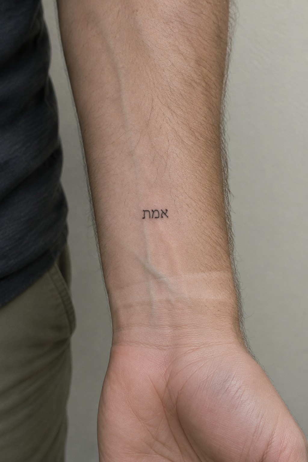 Hairy forearm in gray shirt with small Hebrew tattoo above fist