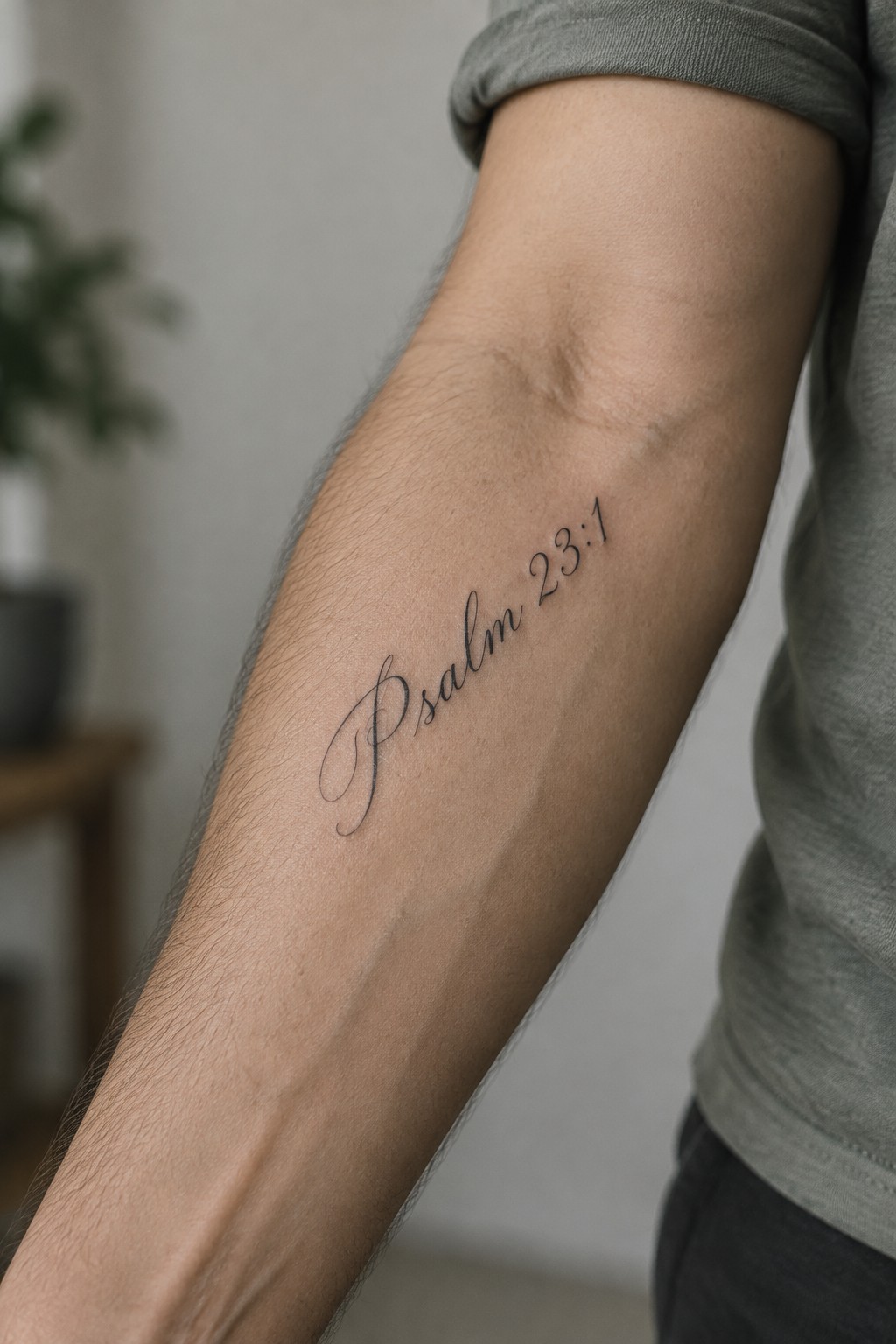 A close up of a man's forearm showing a small cursive tattoo that reads Psalm 23:1